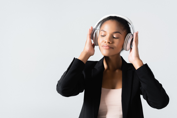 femme d'affaires afro-américaine écoutant de la musique dans des écouteurs isolés sur gris - Photo, image