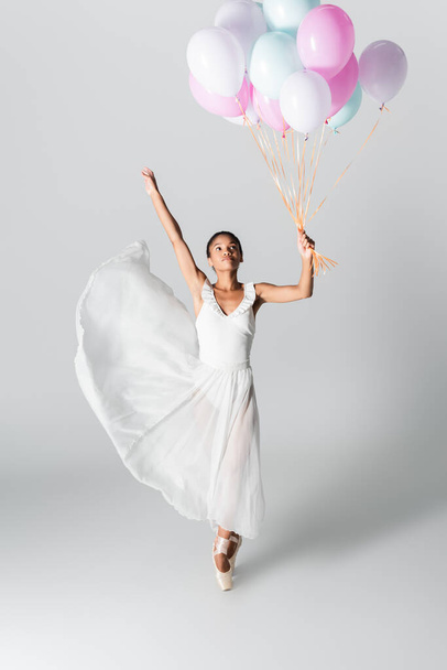graceful african american ballerina in dress dancing with balloons on white background - Foto, Bild