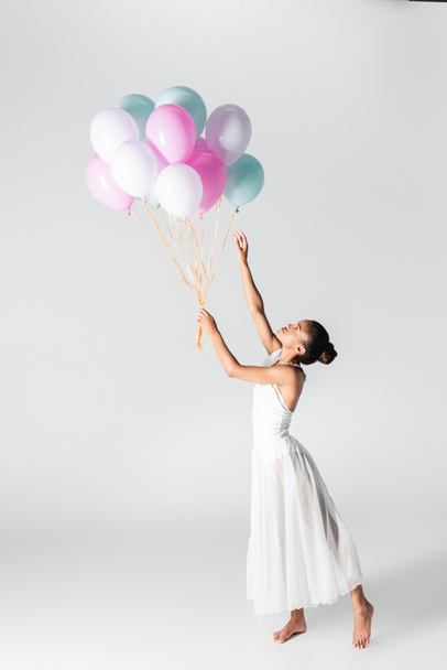 barefoot graceful african american ballerina in dress with balloons on white background - Fotó, kép