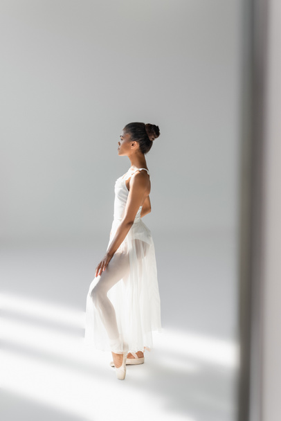 boční pohled na půvabný africký americký balerína v šatech na bílém pozadí - Fotografie, Obrázek