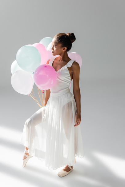 graceful african american ballerina in dress with balloons on white background - Photo, Image