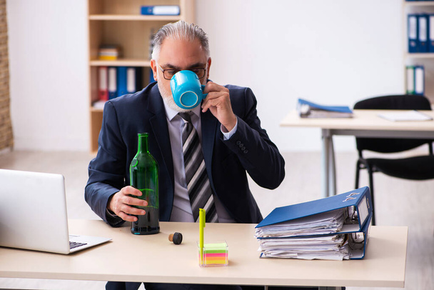 Old male employee drinking alcohol in the office - Fotografie, Obrázek