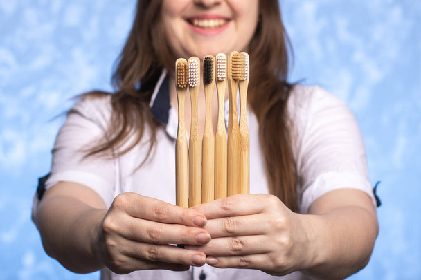 many bamboo toothbrushes in female hands close-up. girl with a defocused smile. environmentally friendly biodegradable hygiene items. multi-colored bristles. place for text. horizontal photo - Photo, Image