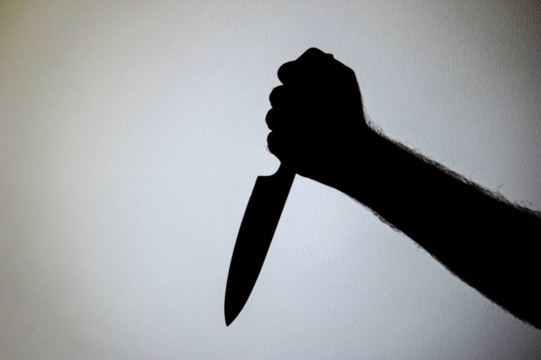 Bıçak tutan bir erkek kolunun duvarına yansıtılmış siluet.. - Fotoğraf, Görsel