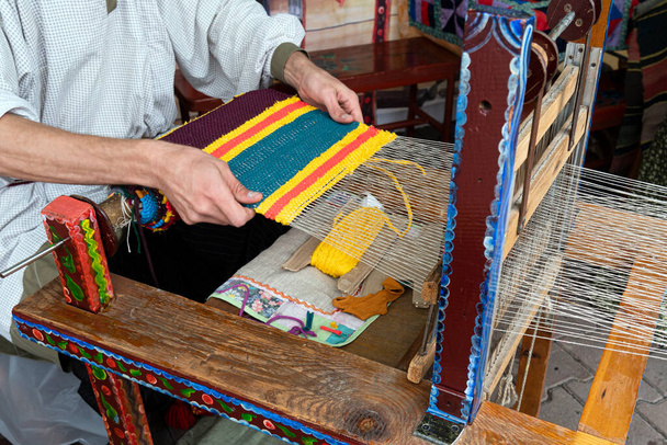Руки человека ткут ткань на деревянном ткацком станке. Традиционное русское народное искусство. Процесс ковроткачества. - Фото, изображение