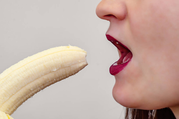 Fragment van de lippen van een vrouw die zich klaarmaakt om een banaan te eten, een seksuele connotatie - Foto, afbeelding