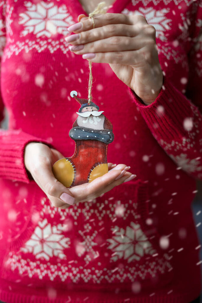 Belle mani femminili in un maglione rosso con un modello tenere un ciondolo in legno sotto forma di Babbo Natale in uno stivale. - Foto, immagini