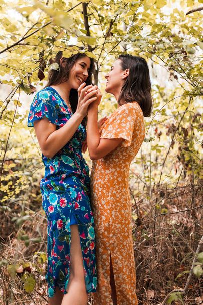 Ormanda birbirini okşayan iki genç lezbiyen uzun elbiseler giyiyor. - Fotoğraf, Görsel