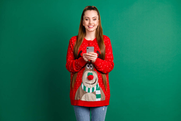 Photo of attractive charming lady hold telephone device read newyear congrats good mood wear red ugly ornament deer reindeer sweater pullover jeans isolated green color background - Foto, Imagem