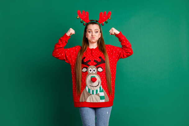 Photo of attractive funky childish lady long brown tail showing biceps arms fists pushing hold breath childish wear deer horns headwear red ornament pullover isolated green color background - Φωτογραφία, εικόνα