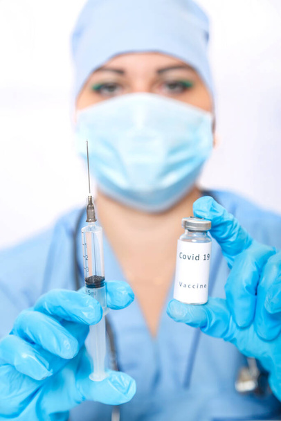 A vial with a vaccine against the virus and a syringe in the hands of a masked doctor. Vertical photo - 写真・画像