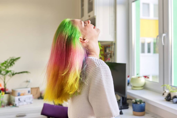 Fashionable teen girl with trendy rainbow dyed hair combing hair at home - Fotó, kép