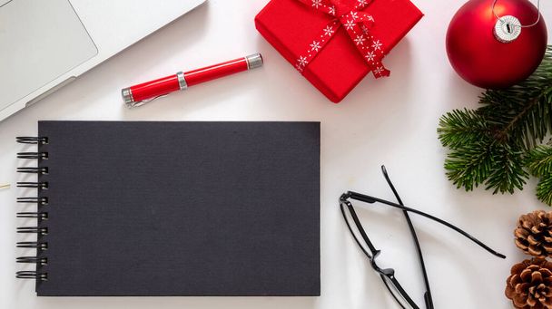 Christmas, office closed. Business desk flat lay, holiday card template. Blank black notebook, laptop and red color xmas decoration on white background, top view - Photo, Image