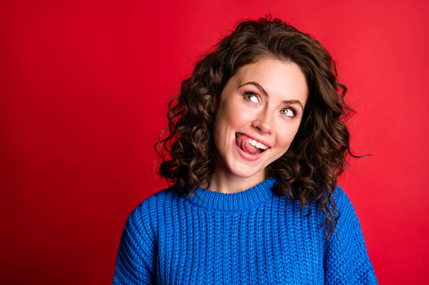 Closeup photo of funky lovely cute lady curly hairstyle stick out tongue licking teeth interested look up empty space wear blue knitted sweater pullover isolated red color background - Valokuva, kuva