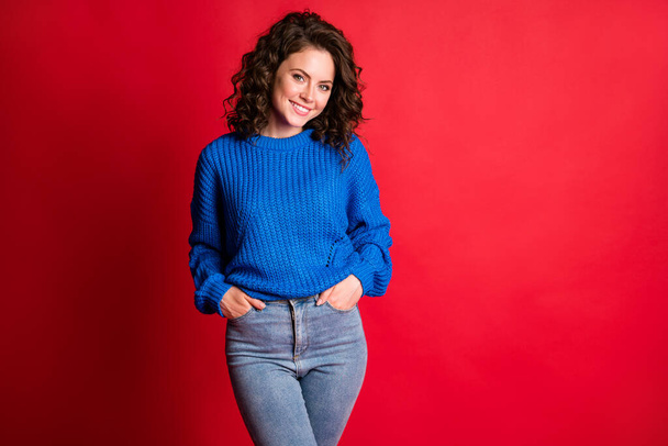 Photo of lovely cute lady curly wavy hairstyle hands pockets confident self-assured beaming smile wear blue knitted sweater pullover jeans isolated red color background - Foto, Bild