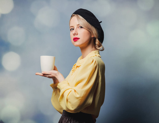 Красивая девушка в винтажной одежде с чашкой кофе на сером фоне - Фото, изображение