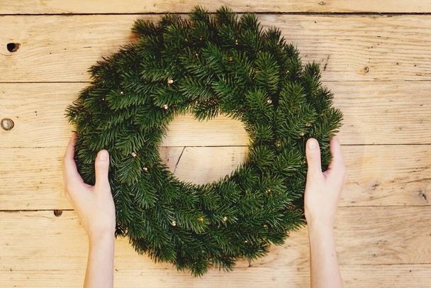Woman hands holding Christmas wreath on wooden background. - Foto, Bild