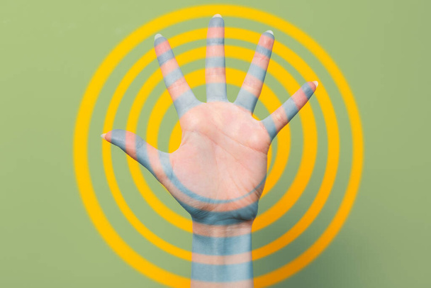 La mano de una mujer con los dedos extendidos. Fondo verde con anillos amarillos. De cerca. Concepto de hipnosis, influencia y psicología. - Foto, Imagen