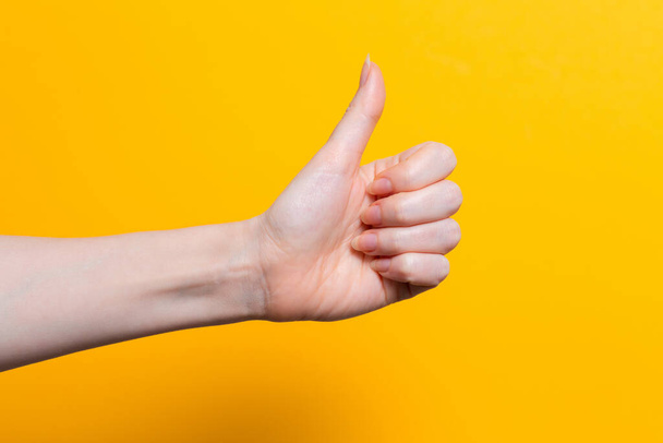 A woman's hand gives a thumbs up. Close up. Yellow background. Copy space. - Фото, изображение
