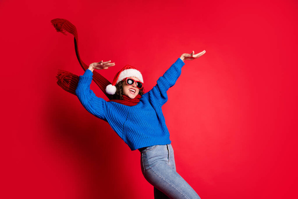 Photo portrait of girl having fun at party dancing holding hands arms up wearing eyeglasses blue pullover scarf santa hat isolated on bright red background - Photo, image