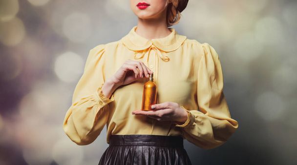 Όμορφο κορίτσι σε vintage ρούχα με μπουκάλι άρωμα σε γκρι φόντο - Φωτογραφία, εικόνα