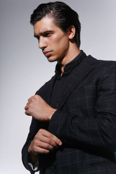 Primer plano retrato de un joven guapo y serio en traje negro sobre fondo blanco oscuro. Vista vertical. - Foto, imagen