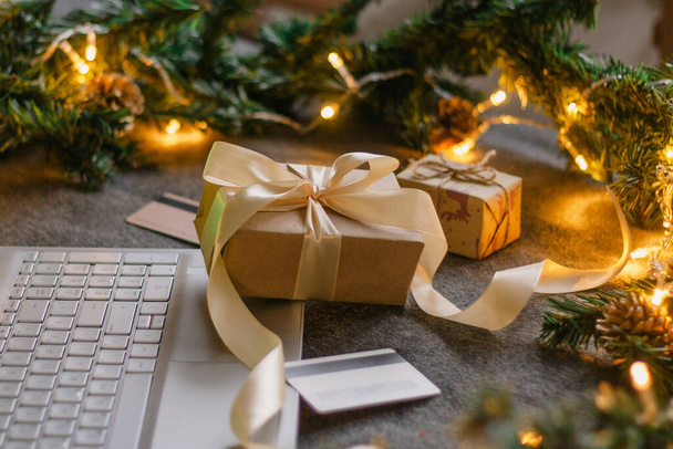 Christmas shopping online with a credit card for the holiday. Laptop with gifts on the table next to fir branches and a garland of lights. - Photo, image