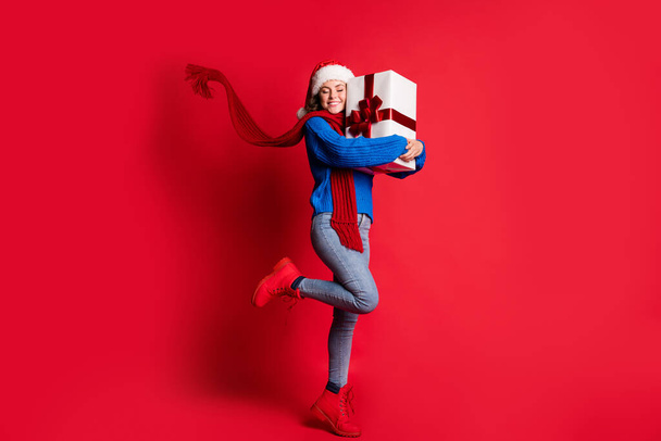 Photo portrait full body cheerful woman hugging present box smiling closed eyes standing on one leg scarf flowing isolated on bright red colored background - Photo, Image