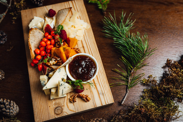 Piatto di formaggio servito con uva, marmellata, fichi, cracker e noci su uno sfondo di legno con decorazioni naturali - Foto, immagini