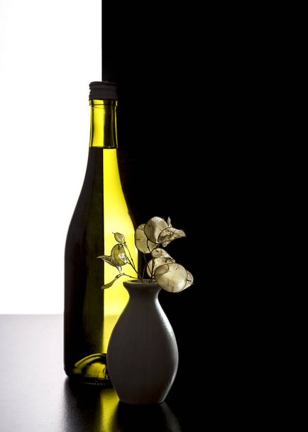 Бутылка и ваза с сушеными цветами на черно-белом фоне. - Фото, изображение