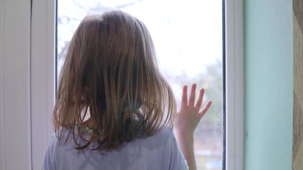 A girl stands in front of the window and knocks on the glass with her palm 4k - Photo, image