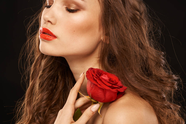 žena s červenou růží na tmavém pozadí dlouhé vlasy make-up červené rty - Fotografie, Obrázek