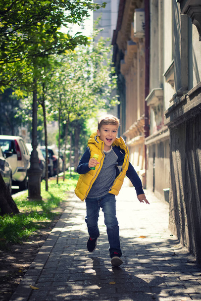 Happy kid having fun and running on the street. Playful boy running on a sidewalk towards the camera.  - Foto, Imagen