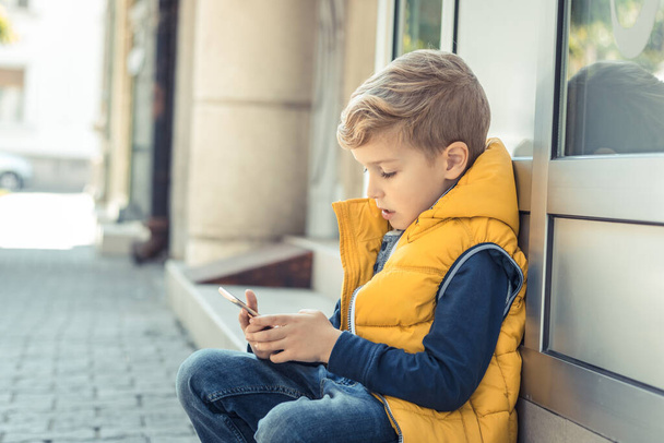 Malý chlapec relaxovat ve městě a hrát hry na chytrý telefon.  - Fotografie, Obrázek