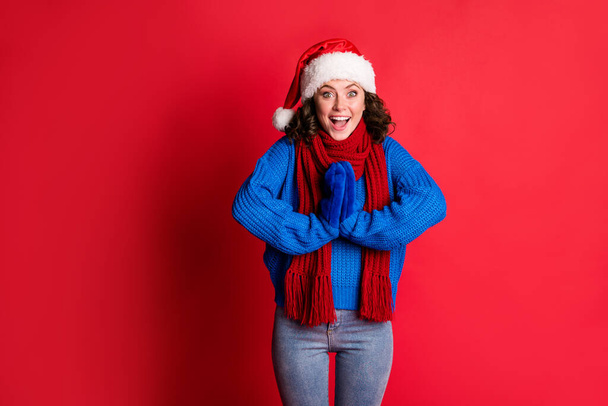 Photo portrait excited amazed girl waiting open present wondering whats inside holding hands together clapping wearing blue pullover scarf santa hat isolated vivid red colored background - Fotoğraf, Görsel