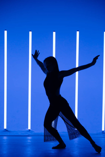 Silhouette of a attractive young woman dancer dancing in a room with neon lamps. Sporty beautiful girl model enjoys a dance in the studio with neon amazing color. - Foto, Imagen