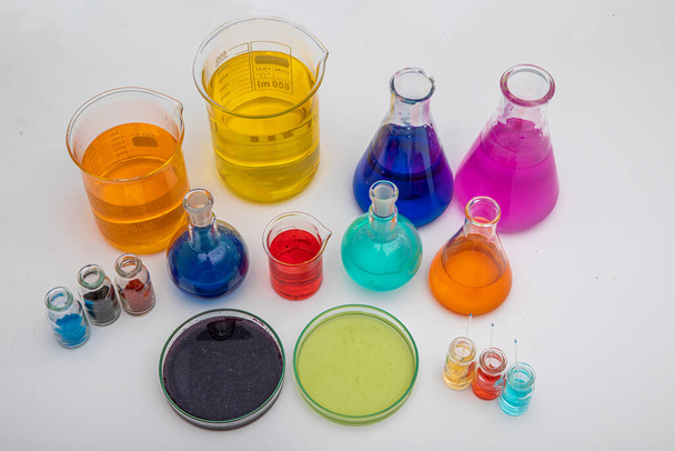 Laboratorium glaswerk met vloeistoffen van verschillende kleuren op witte tafel. Volumetrisch laboratoriumglaswerk op witte achtergrond. - Foto, afbeelding