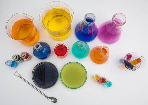 Laborgläser mit Flüssigkeiten in verschiedenen Farben auf weißem Tisch. Volumetrische Laborgläser auf weißem Hintergrund. - Foto, Bild
