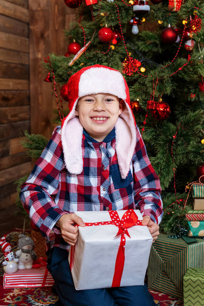 όμορφο αγοράκι δίπλα στο χριστουγεννιάτικο δέντρο είναι ευτυχισμένο με ένα δώρο - Φωτογραφία, εικόνα