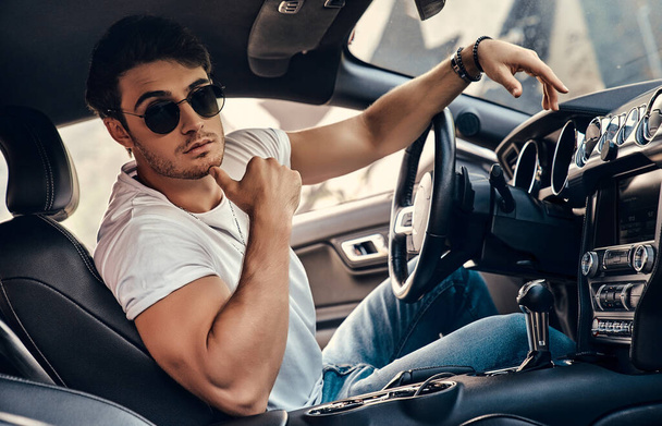 Handsome young man in sunglasses and casual clothes sitting in his modern sport car - Φωτογραφία, εικόνα
