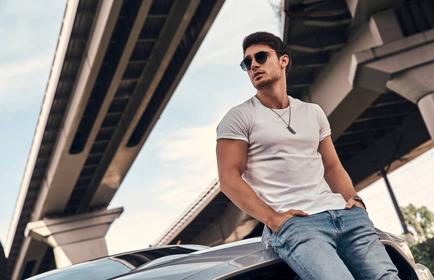 Handsome young man in casual clothes standing near his modern sport car on the street - Foto, immagini