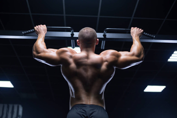 Handsome young muscular man of model appearance working out training pumping up back muscles in the gym gaining weight on machines - Fotoğraf, Görsel