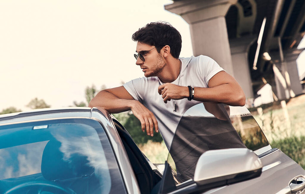 Handsome young man in casual clothes standing near his modern sport car on the street - Foto, Imagen