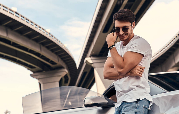 Handsome young man in casual clothes standing near his modern sport car on the street - Foto, imagen