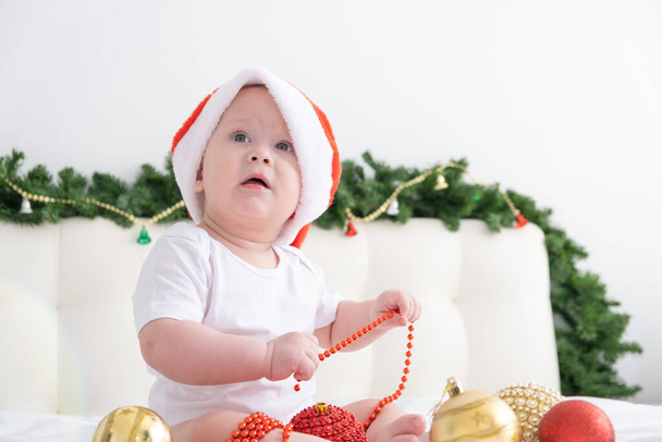 mignon bébé garçon dans le chapeau de Père Noël sur le lit avec literie blanche à la maison avec des décorations de Noël. - Photo, image