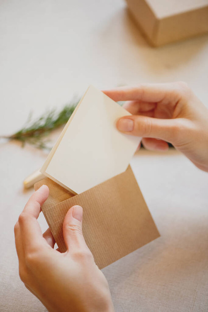 Close up of female hands putting a card into a craft paper envelope. - Photo, image