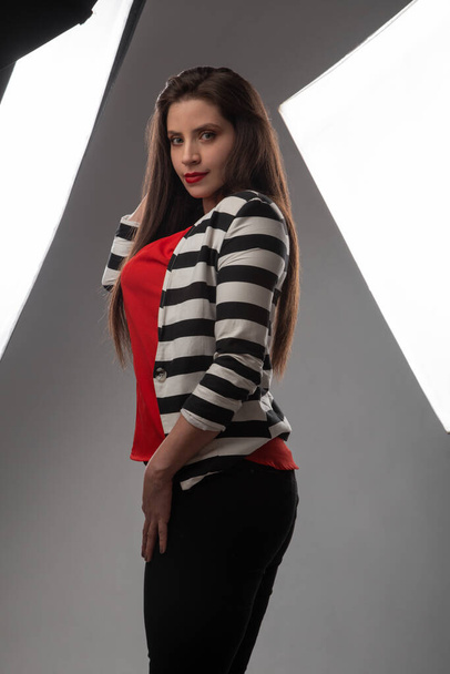 Uzun saçlı, kırmızı bluz ve ceket giyen beyaz tenli genç bir kadının fotoğraf çekimi. Profesyonel ışıklarla dolu bir stüdyoda çekilmiş bir fotoğraf. - Fotoğraf, Görsel