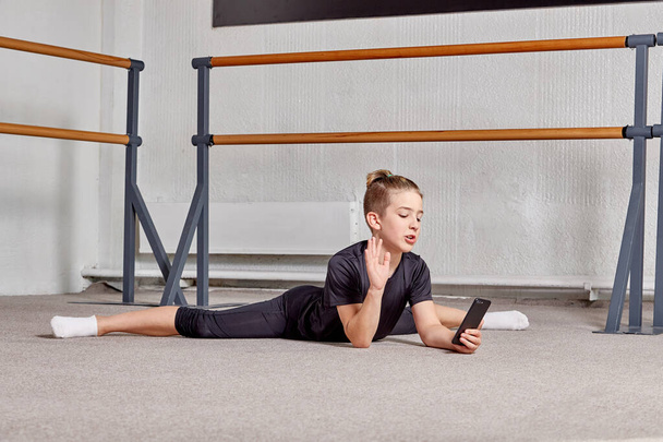 A man is lying on the floor on the splits in the gym and holding a smartphone. - Zdjęcie, obraz