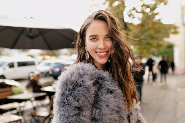 Mujer de moda feliz con el pelo ondulado vestido abrigo de piel mirando a la cámara con sonrisa. Foto de alta calidad - Foto, imagen