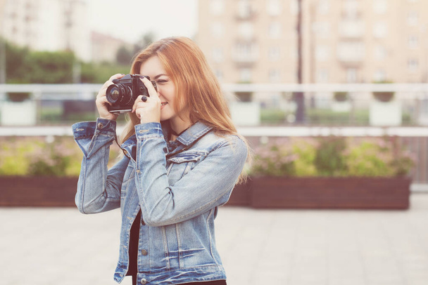 Молода дівчина фотограф ходить по вулиці в джинсовій куртці зі старою камерою
 - Фото, зображення